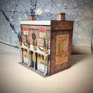 May include: A paper model of a brick building with a storefront decorated for Christmas. The building has a sign that reads "For Superior Cleansing, Calvert's No. 5 Carbolic Soap".