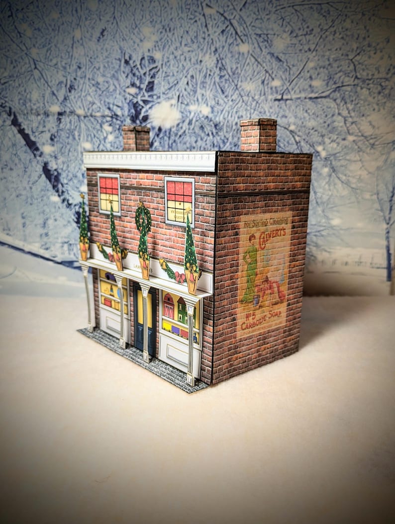 May include: A paper model of a brick building with a storefront decorated for Christmas. The building has a sign that reads "For Superior Cleansing, Calvert's No. 5 Carbolic Soap".