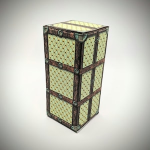 Puede incluir: Una pequeña caja rectangular de madera con un diseño estampado verde y dorado. La caja tiene detalles metálicos y una tapa con bisagras.