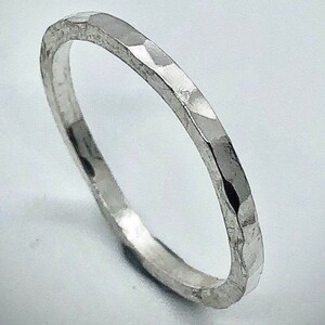 May include: A silver ring with a hammered texture. The ring is thin and has a faceted surface, reflecting light. The ring is a simple band, suitable for everyday wear.