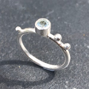 May include: A silver ring with a light blue gemstone and three small silver beads.