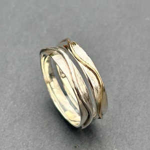 May include: Two intertwined silver rings with a thin gold band on one ring. The rings have a wavy, organic design.