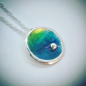 May include: A silver pendant necklace with a round, blue, green, and yellow enamel pendant with a small silver bead in the center.