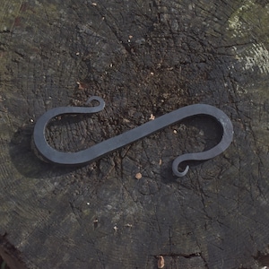 Könnte beinhalten: Ein schwarzer Feuerstarter aus Metall mit einem einzigartigen S-förmigen Design und gekräuselten Enden. Der Feuerstarter liegt auf einer Holzoberfläche.