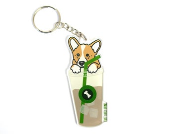 May include: A brown and white corgi dog peeks out of a green and white iced coffee cup with a straw. The cup has a bone and ice cubes inside. The keychain is made of acrylic and has the text "That Corgi Life" on the side.