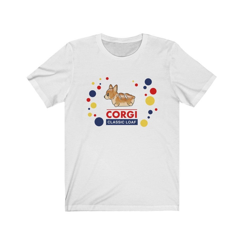 May include: White t-shirt with a cartoon corgi dog illustration in the center. The corgi is brown and white with a red collar and is surrounded by colorful dots. The text "Corgi Classic Loaf" is below the dog.