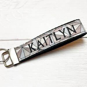 May include: A black and white geometric patterned key chain with the name "KAITLYN" embroidered in black thread.