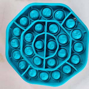 May include: A turquoise octagonal fidget toy with alphabet letters. The toy has a series of circular bubbles, each with a letter of the alphabet. The letters are in a white font. The toy is made of a soft, flexible material.