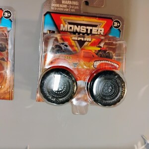 May include: Orange and yellow Monster Jam truck toy in a clear plastic package. The truck has large black tires and the name "Pro Loco" printed on the side. The package has the Monster Jam logo and a warning about small parts.
