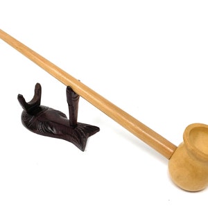 Könnte beinhalten: Eine Holzpfeife mit einem langen, schlanken Schaft und einer abgerundeten Schale. Die Pfeife liegt auf einem fischförmigen Holzständer.