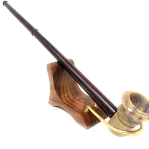 Könnte beinhalten: Eine Holzpfeife mit braunem Schaft und einem Keramikkopf. Die Pfeife liegt auf einem Holzständer.