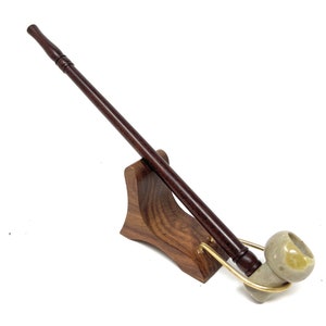 May include: A wooden smoking pipe with a brown stem and a light green ceramic bowl. The pipe is displayed on a wooden stand.
