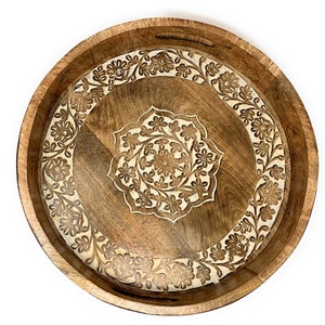 K&ouml;nnte beinhalten: Ein rundes Holztablett mit einem geschnitzten Blumenmuster. Das Tablett ist braun mit einer helleren Holzeinlage.