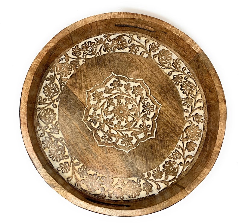 K&ouml;nnte beinhalten: Ein rundes Holztablett mit einem geschnitzten Blumenmuster. Das Tablett ist braun mit einer helleren Holzeinlage.