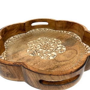 K&ouml;nnte beinhalten: Ein rundes Serviertablett aus Holz mit einem geschnitzten Blumenmuster. Das Tablett hat zwei Griffe an den Seiten und ist aus hellbraunem Holz gefertigt.