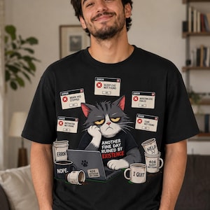 May include: A black t-shirt featuring a graphic of a grumpy cat sitting at a laptop. The design includes multiple error message pop-ups reading "Sleep.exe not found," "Brain has stopped," "Adulting.exe failed," and "Care not found," with the text "Another fine day ruined by existence."