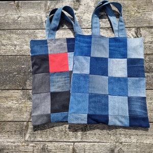 Op de afbeelding: Twee blauwe denim tassen met patchwork-ontwerpen. Eén tas heeft een rood vierkant in het midden. Beide tassen hebben een geruit patroon.