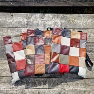 Op de afbeelding: Drie patchwork leren tassen met zwarte banden. De tassen zijn gemaakt van verschillende gekleurde lederen vierkanten, waaronder bruin, beige, rood, wit en grijs.