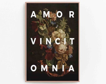 May include: A rectangular wall art print in a thin copper frame featuring a dark floral still life painting with a bouquet of flowers and a butterfly. The white text AMOR VINCIT OMNIA is centered in capital letters over the floral arrangement.