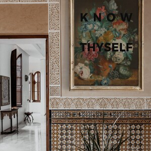 May include: A framed rectangular wall art piece featuring a colorful floral bouquet in a vase with the black text KNOW THYSELF centered over the image. The artwork is displayed on a wall with intricate carved plaster and patterned tile details.