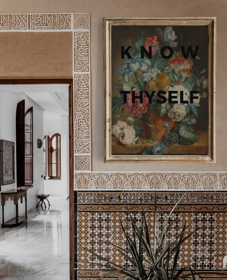 May include: A framed rectangular wall art piece featuring a colorful floral bouquet in a vase with the black text KNOW THYSELF centered over the image. The artwork is displayed on a wall with intricate carved plaster and patterned tile details.