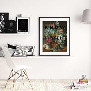 May include: A framed wall art print featuring a classical floral still life painting in a dark vase, overlaid with the bold black text "KNOW THYSELF" in a sans-serif font. The artwork is displayed in a black frame on a white wall shelf.