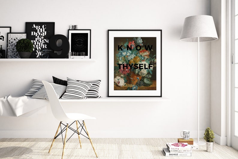 May include: A framed wall art print featuring a classical floral still life painting in a dark vase, overlaid with the bold black text "KNOW THYSELF" in a sans-serif font. The artwork is displayed in a black frame on a white wall shelf.