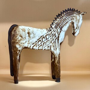 May include: A ceramic horse figurine in a standing pose. The horse is primarily white with brown accents, including the mane, tail, and legs. The body features a diamond pattern. The sculpture has a rustic, handcrafted appearance.