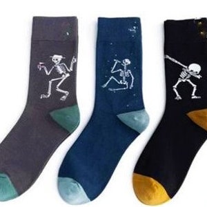 Puede incluir: Tres pares de calcetines novedosos con dise&ntilde;os de esqueletos. Un par es gris oscuro, otro azul marino y el tercero negro. Cada calcet&iacute;n tiene una pose de esqueleto diferente. Cada par tiene una puntera y un tal&oacute;n de diferente color.