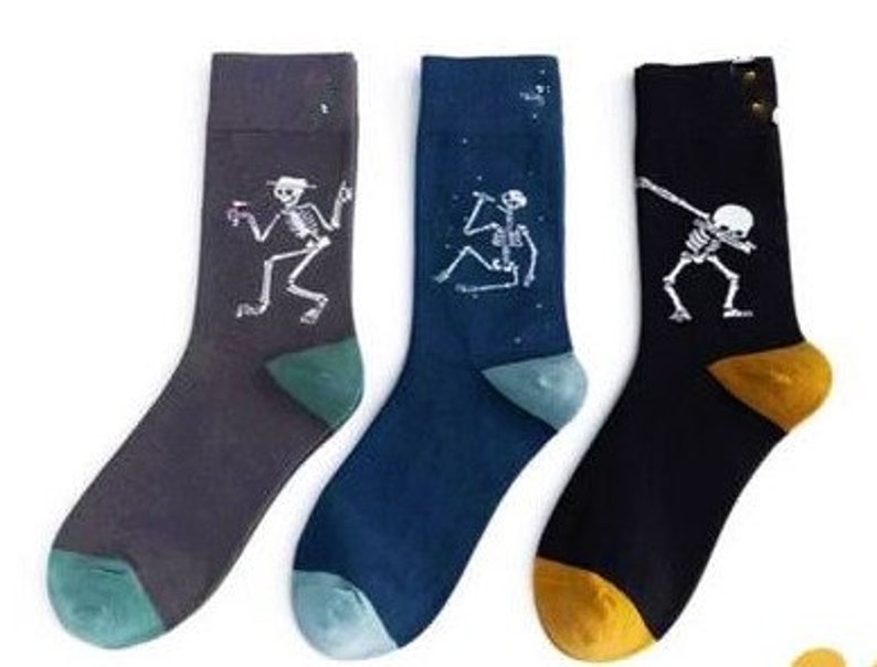 Puede incluir: Tres pares de calcetines novedosos con dise&ntilde;os de esqueletos. Un par es gris oscuro, otro azul marino y el tercero negro. Cada calcet&iacute;n tiene una pose de esqueleto diferente. Cada par tiene una puntera y un tal&oacute;n de diferente color.