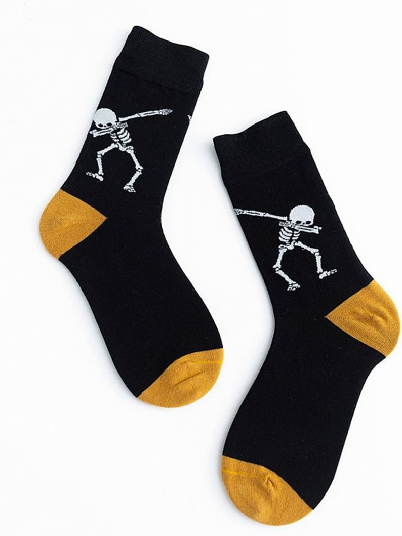 Puede incluir: Un par de calcetines negros con un dise&ntilde;o de esqueleto blanco haciendo un dab. Los talones y las puntas son dorados. Estos calcetines probablemente est&aacute;n hechos de un material suave y c&oacute;modo.