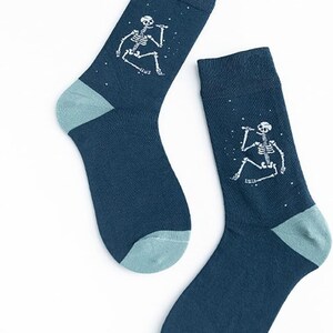 Puede incluir: Un par de calcetines azul oscuro con talones y dedos de los pies de color verde azulado claro. Cada calcet&iacute;n presenta un gr&aacute;fico de esqueleto blanco con un micr&oacute;fono, rodeado de peque&ntilde;os puntos blancos. Los calcetines probablemente est&aacute;n hechos de un material suave y c&oacute;modo.