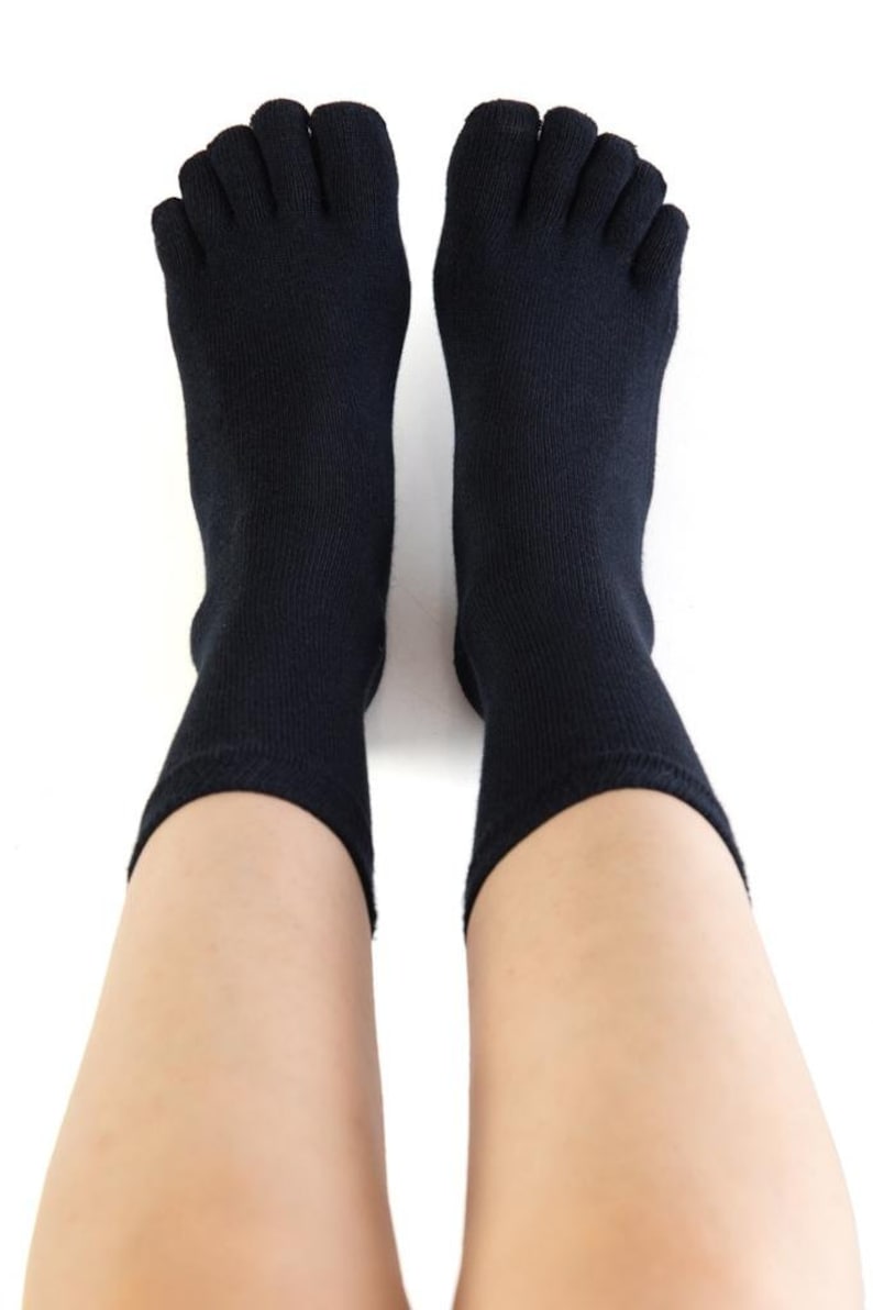 May include: A pair of black toe socks with five individual toe compartments. The socks are worn on a person's feet.