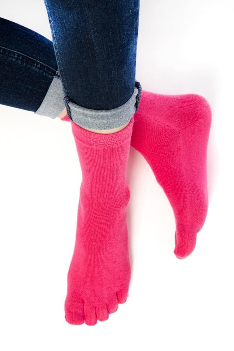 May include: A pair of pink toe socks with five individual toe compartments. The socks are made of a soft, stretchy material and are worn on a person's feet.