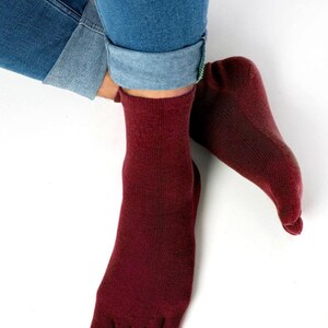 May include: A pair of maroon toe socks with a ribbed texture. The socks are worn on a person's feet, with the toes of the socks visible.
