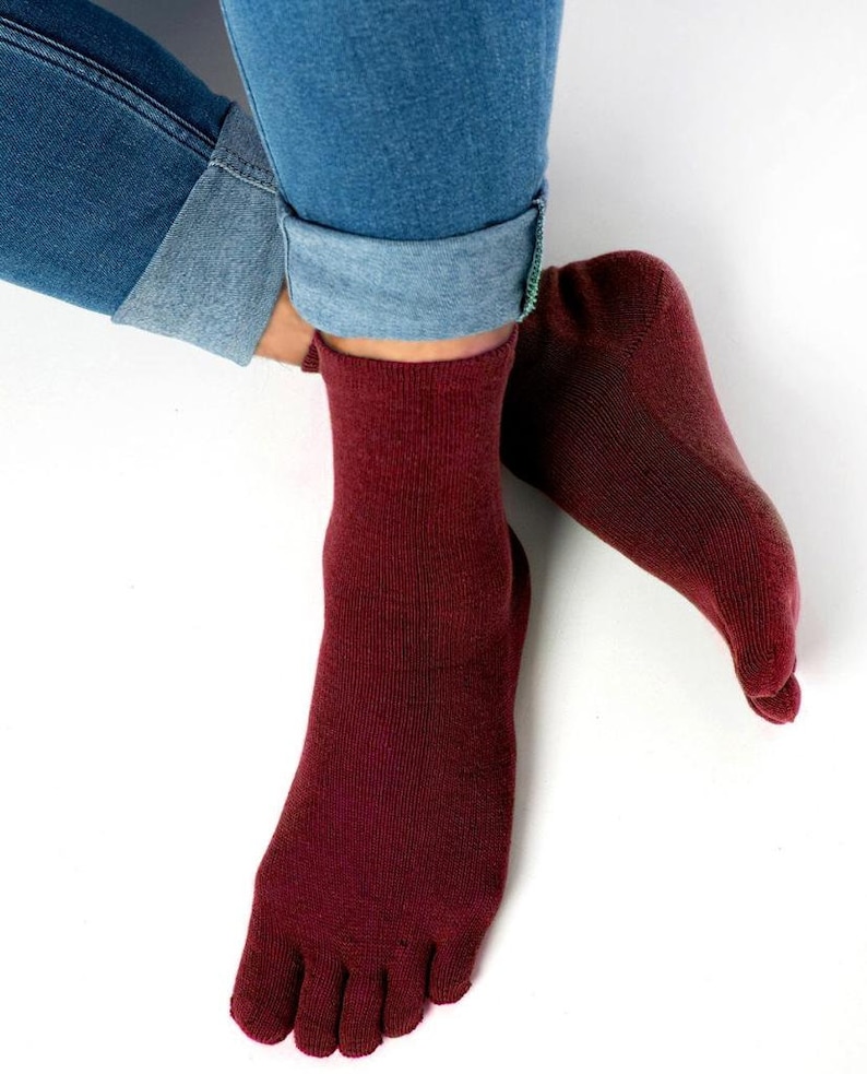 May include: A pair of maroon toe socks with a ribbed texture. The socks are worn on a person's feet, with the toes of the socks visible.