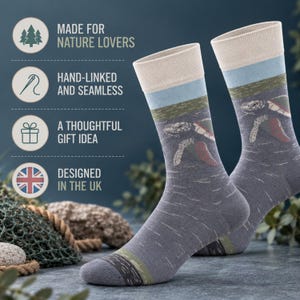Puede incluir: Un par de calcetines grises con un gráfico de tortuga marina, una banda azul claro y un puño color crema. El texto a la izquierda dice: MADE FOR NATURE LOVERS, HAND-LINKED AND SEAMLESS, A THOUGHTFUL GIFT IDEA y DESIGNED IN THE UK.