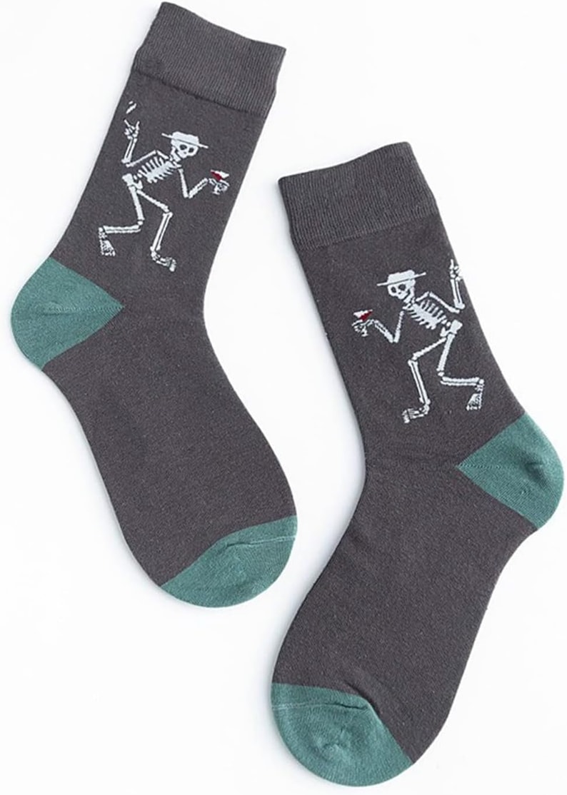 Puede incluir: Un par de calcetines gris oscuro con tal&oacute;n y puntera verde azulado. Cada calcet&iacute;n presenta un gr&aacute;fico de esqueleto blanco con sombrero y bebida. Los calcetines est&aacute;n hechos de un material suave.