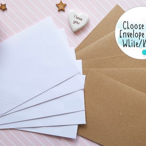 May include: A stack of white envelopes and a stack of brown kraft paper envelopes. A circular white label features the text Choose your Envelope Style! White/Kraft. with a small blue bird illustration. Decorative wooden stars and a heart are present.