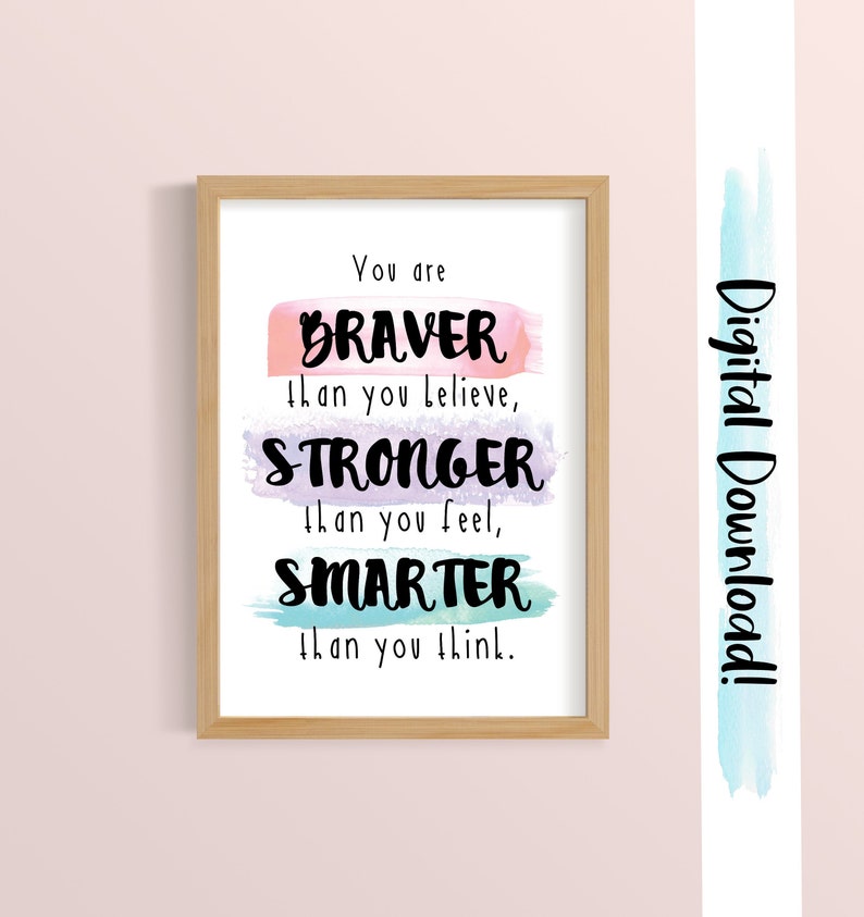 May include: A printable inspirational quote in a wooden frame. The quote reads "You are BRAVER than you believe, STRONGER than you feel, SMARTER than you think." The words are written in black and are layered over watercolor washes in pink, purple, and blue.