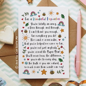 May include: A white card with the message "For a Wonderful Keyworker..." and a heartfelt message. The card is decorated with colorful illustrations of rainbows, bees, suns, and stars. A pink pen rests beside the card.