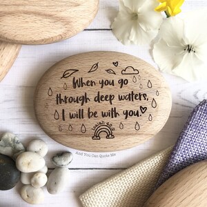 Puede incluir: Un letrero ovalado de madera con la cita "Cuando pases por aguas profundas, estar&eacute; contigo." La cita es de Isa&iacute;as 43:2. El letrero est&aacute; decorado con gotas de lluvia, hojas y un arco&iacute;ris.