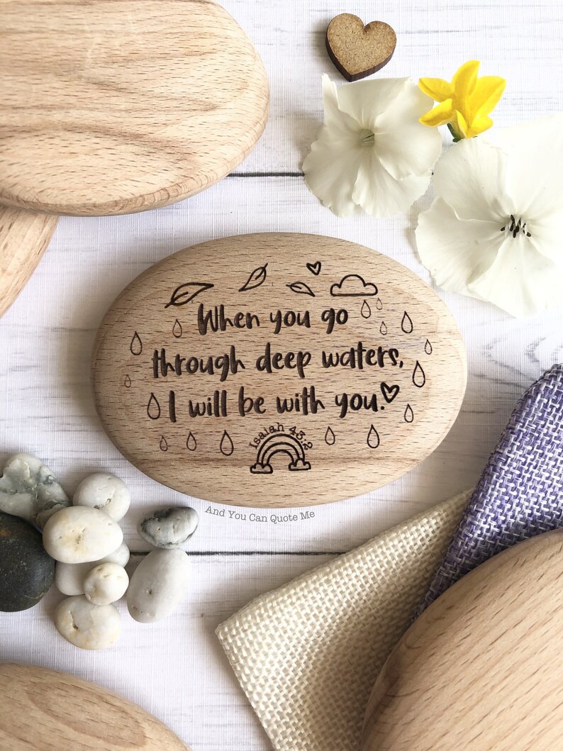 Puede incluir: Un letrero ovalado de madera con la cita "Cuando pases por aguas profundas, estar&eacute; contigo." La cita es de Isa&iacute;as 43:2. El letrero est&aacute; decorado con gotas de lluvia, hojas y un arco&iacute;ris.