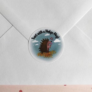 May include: A round sticker with a cartoon hedgehog holding a flower, surrounded by leaves, clouds, and the text "Sent with a Hedge-Hug!". The sticker is on a white envelope.
