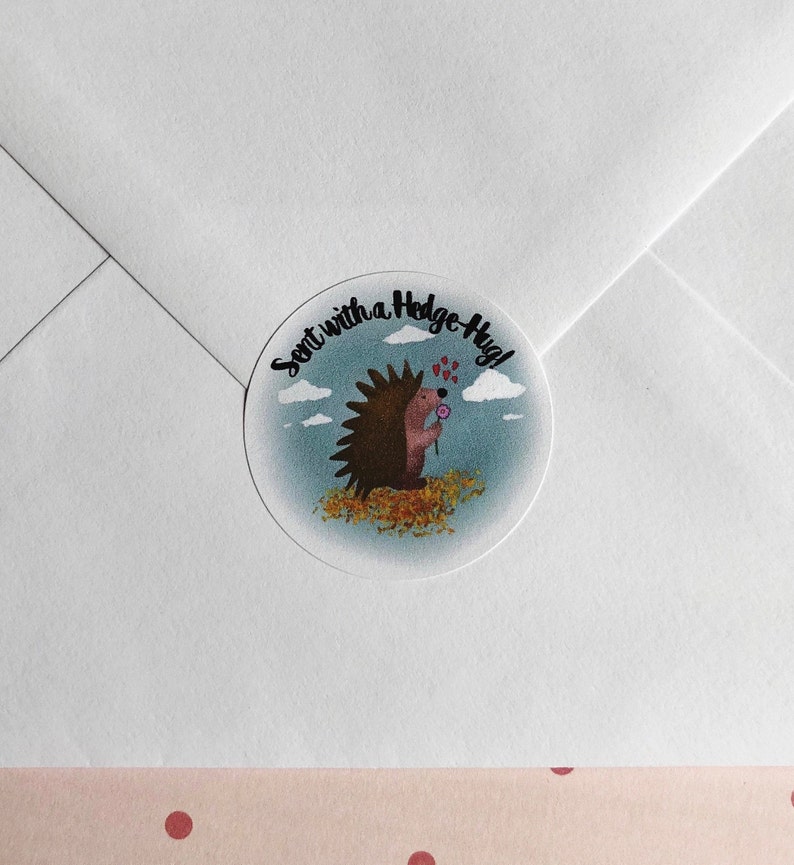 May include: A round sticker with a cartoon hedgehog holding a flower, surrounded by leaves, clouds, and the text "Sent with a Hedge-Hug!". The sticker is on a white envelope.