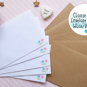 May include: A set of five white envelopes with a blue and pink bird design on the bottom right corner. The envelopes are stacked on top of each other. Next to the envelopes are three brown kraft envelopes. A sign reads "Choose your Envelope Style! White/Kraft."