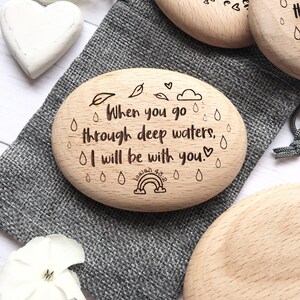 Puede incluir: Piedra de madera grabada con el texto "When you go through deep waters, I will be with you. Isaiah 43:2" con un arco&iacute;ris y gotas de lluvia.