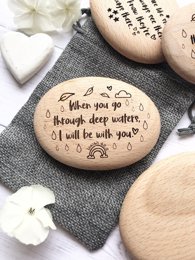 Puede incluir: Piedra de madera grabada con el texto "When you go through deep waters, I will be with you. Isaiah 43:2" con un arco&iacute;ris y gotas de lluvia.