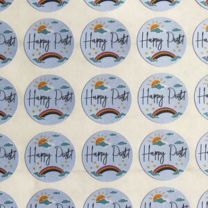 以下が含まれることがあります： 水色の背景に「Happy Post!」の文字が筆記体で書かれた丸いステッカー。各ステッカーには虹、太陽、雲のデザインがあります。ステッカーはグリッドパターンで配置されています。