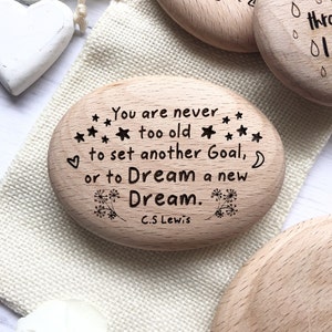May include: A wooden oval-shaped sign with the quote "You are never too old to set another Goal, or to Dream a new Dream." by C.S. Lewis.